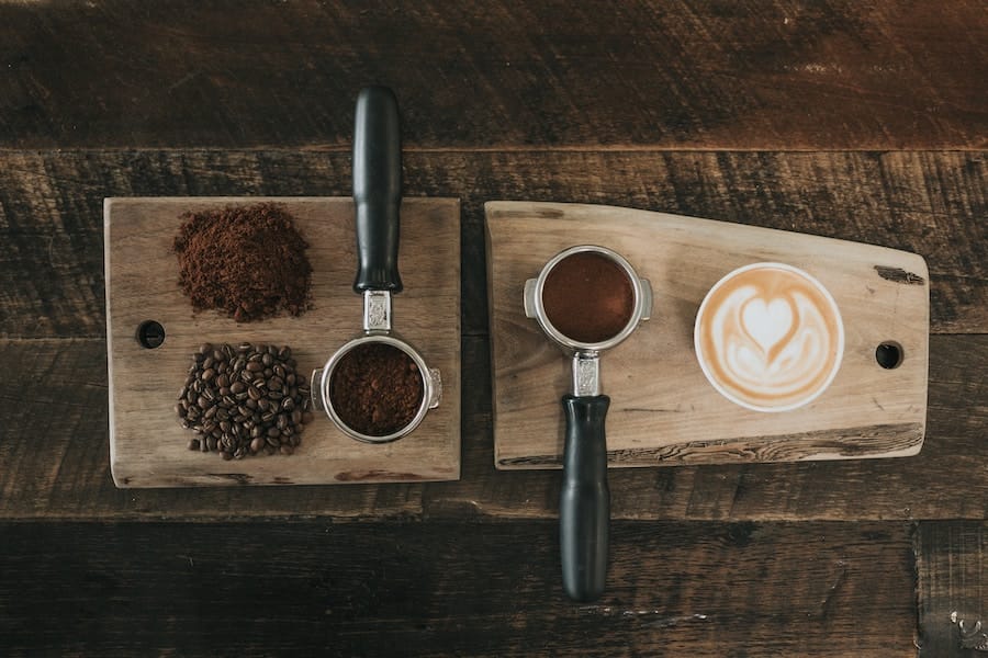 ground coffee, coffee beans, two espresso handles filled, a cup of latte